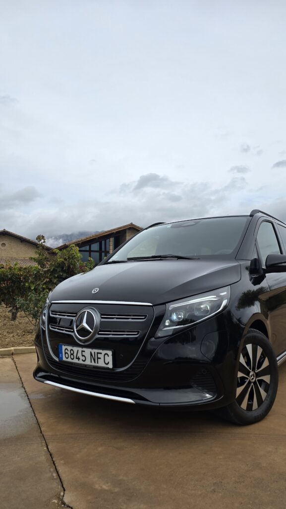 Parte frontal de una Mercedes-Benz V-Class negra aparcada frente a la moderna Bodega Marqués de Riscal, con su distintiva arquitectura ondulada de titanio.