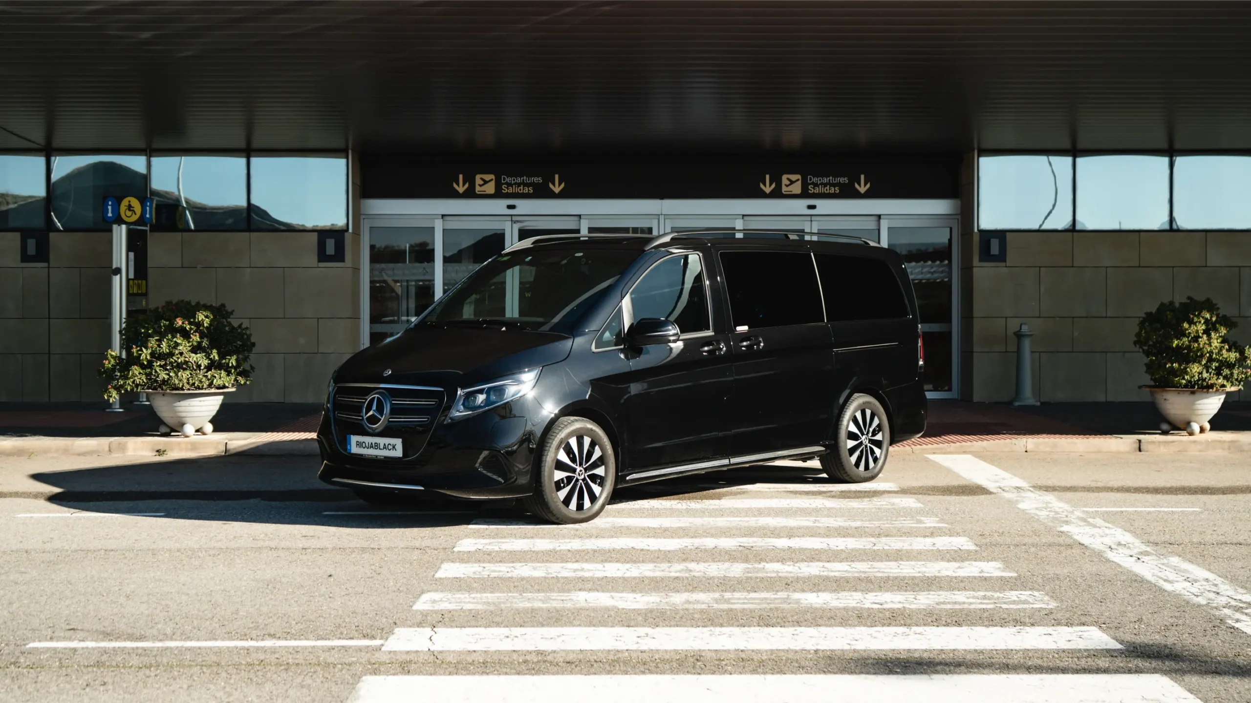 Black Mercedes-Benz EQV luxury van parked at Bilbao Airport terminal for private executive transfers by RiojaBlack.