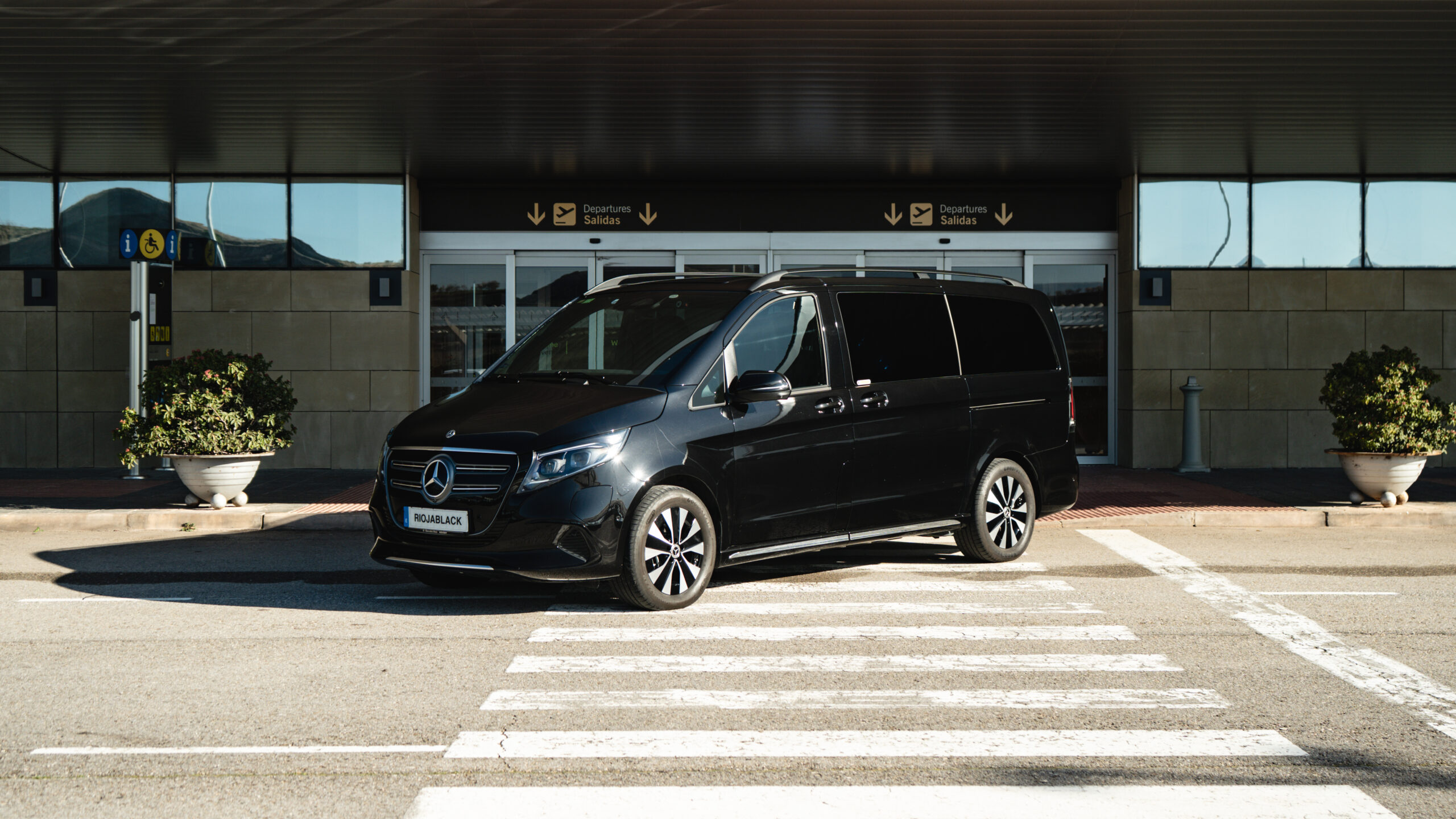 Furgoneta negra Mercedes Clase V de RiojaBlack aparcada en la zona de salidas del aeropuerto, lista para servicios de chófer y taxi de lujo en La Rioja.