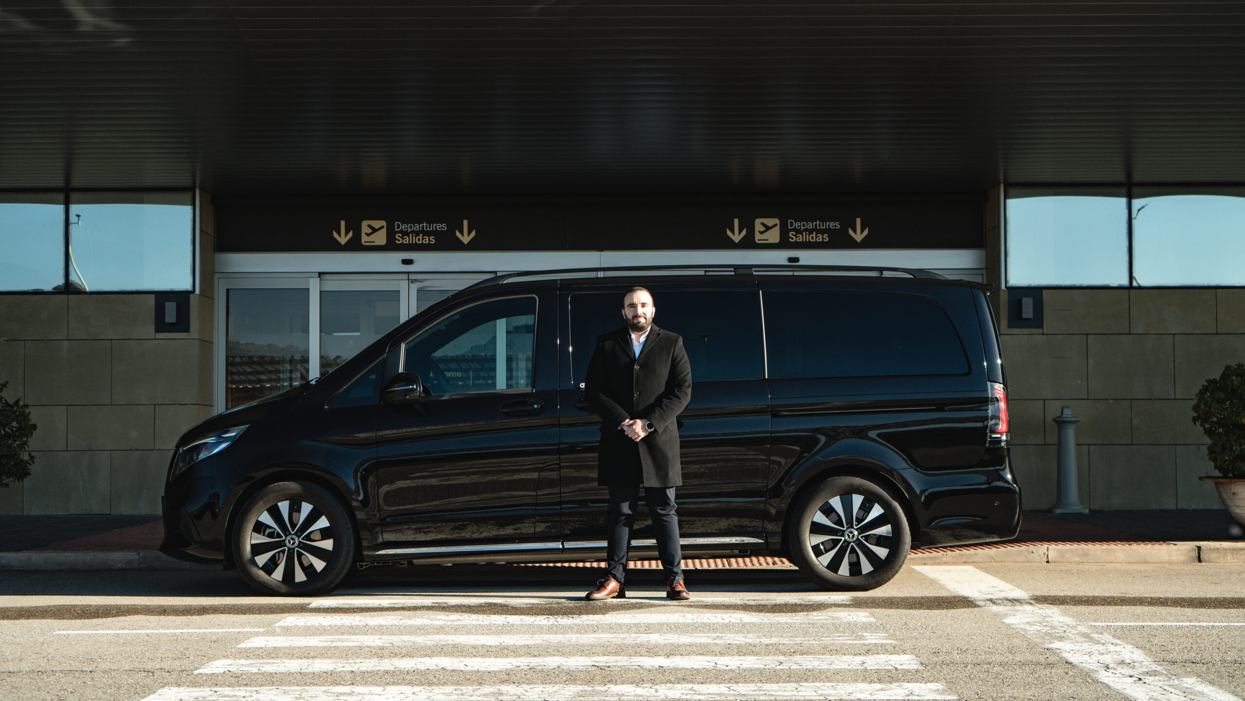 Chófer privado esperando a clientes junto a una furgoneta Mercedes Clase V negra en el aeropuerto de Logroño-Agoncillo.